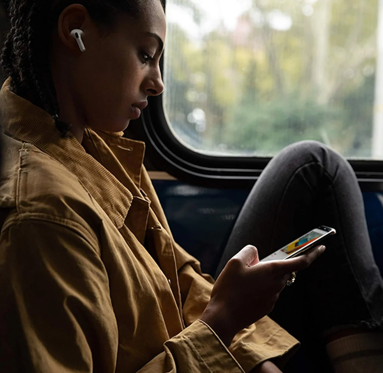Mujer usando airpods pro 1 generación mientras revisa su teléfono en un autobús.