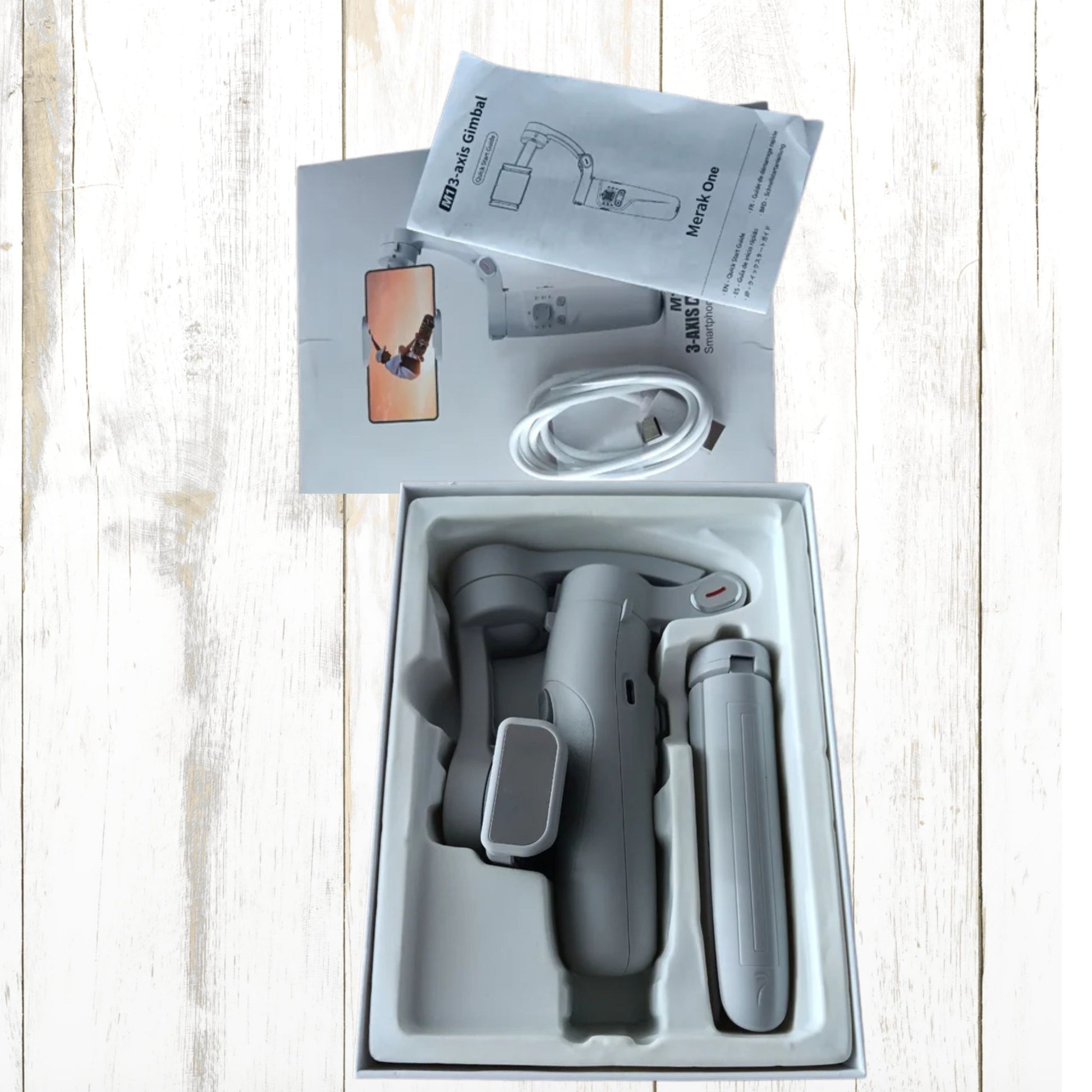 Gimbal estabilizador para móvil en su caja, incluyendo manual y cable, ideal para vídeos estables.